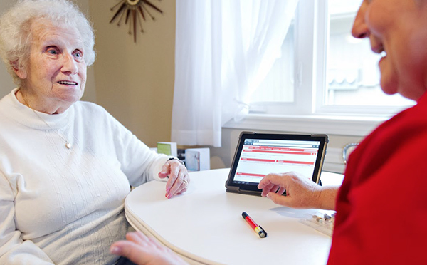 An image showing an elderly lady talking to a health consultant about materials shown on the screen of a tablet.